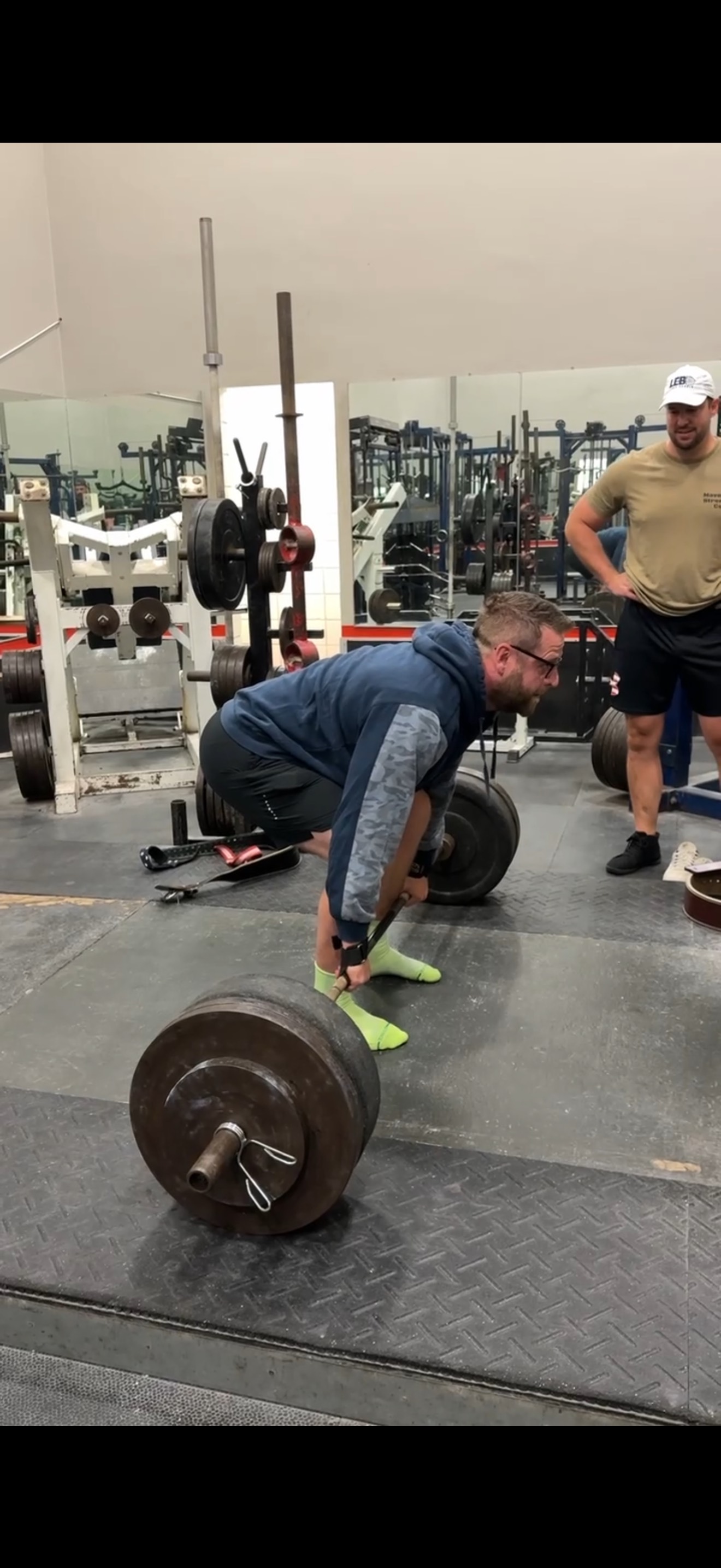 Athlete performing heavy deadlift with coach observing in professional gym